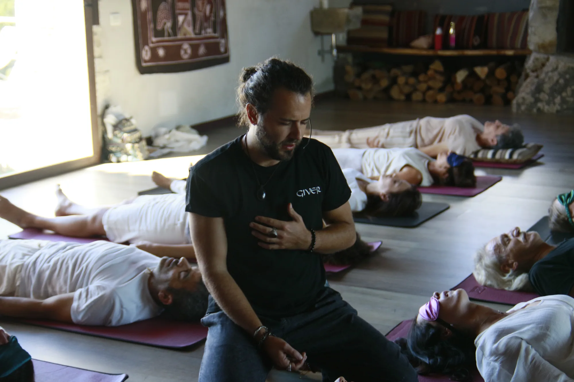 GIVER® facilitator kneeling among participants lying on mats during a Kundalini Activation Astral Work session