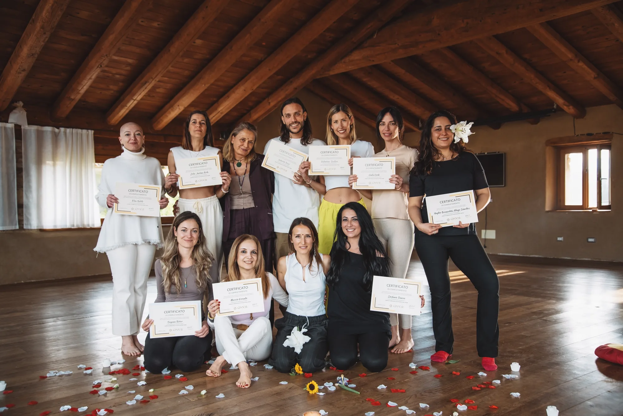 2022 GIVER® Kundalini Activation Astral Work facilitator training graduates holding certificates in a wood-beamed hall in Italy