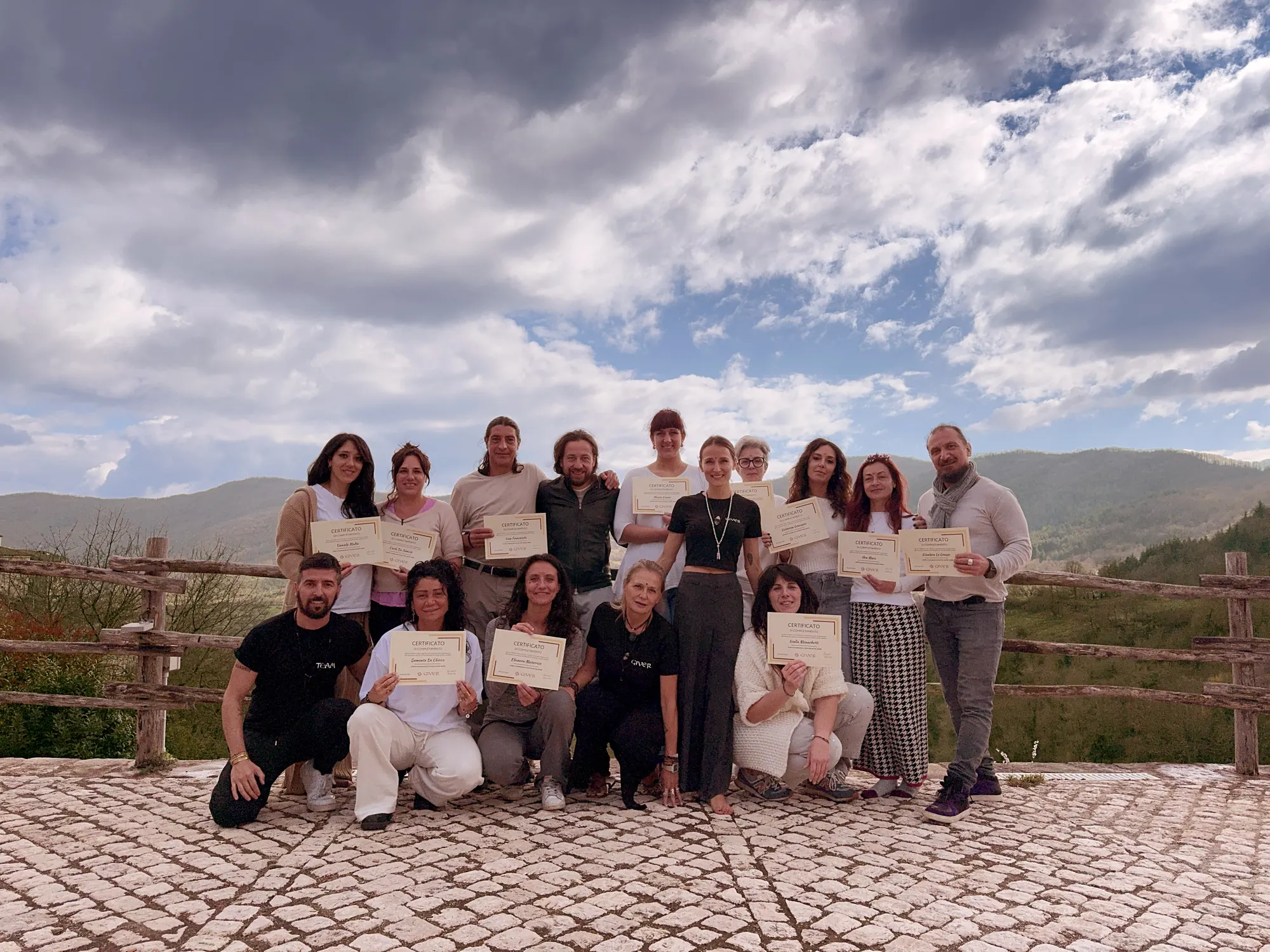 Second 2024 GIVER® facilitator training group receiving certificates on a hilltop terrace in the Italian countryside