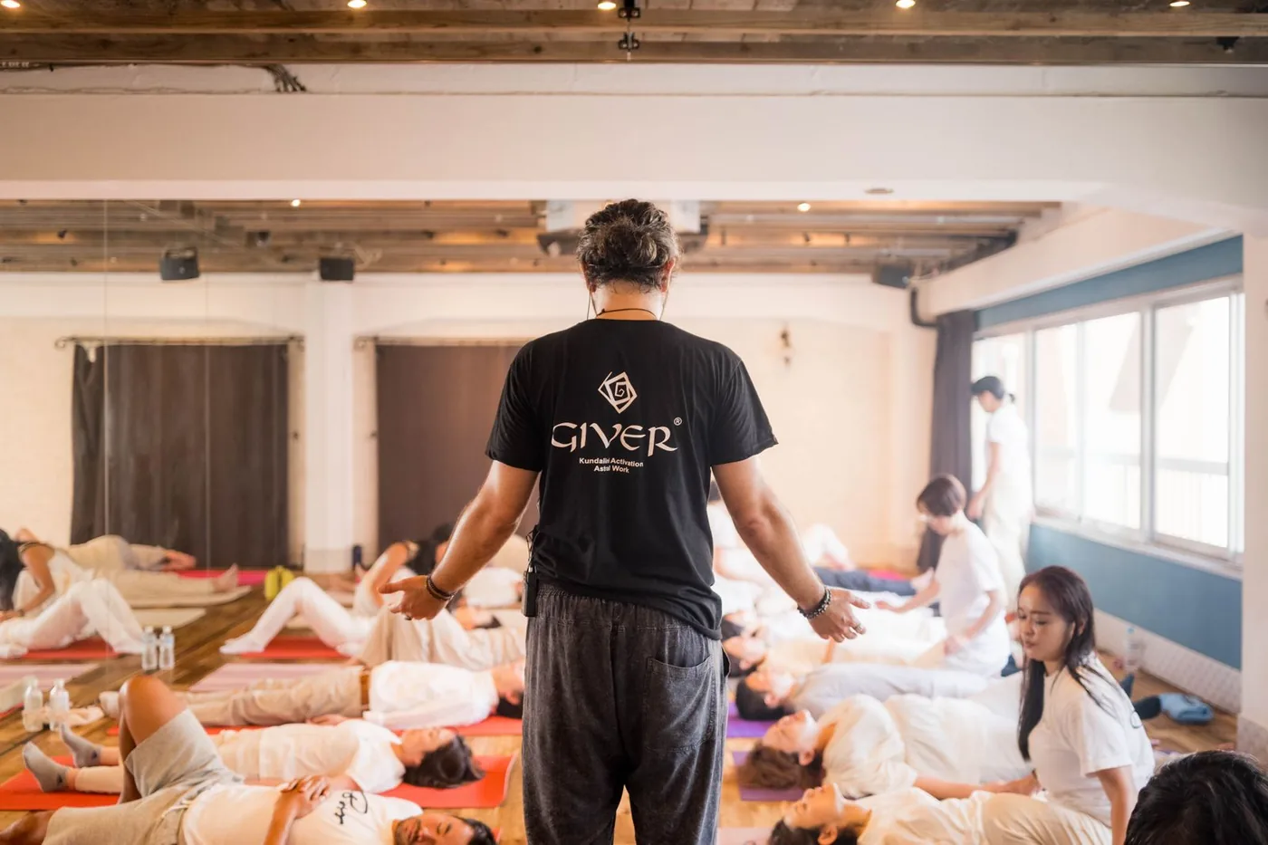 A GIVER® facilitator transmitting energy to participants lying on mats during a Kundalini Activation Astral Work session in Japan